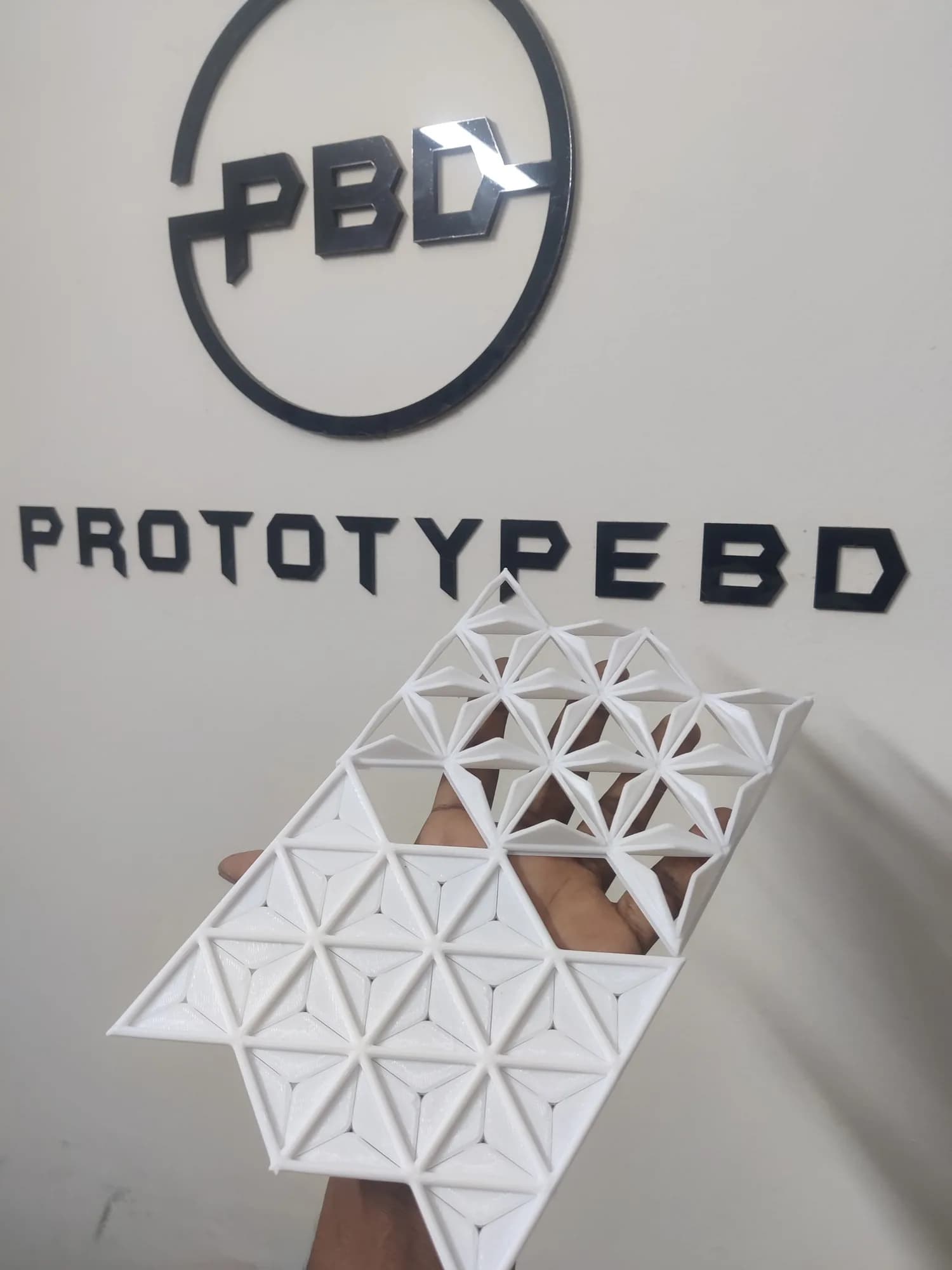 Two printed pattern panels, open and closed, held up in front of the PrototypeBD wall logo