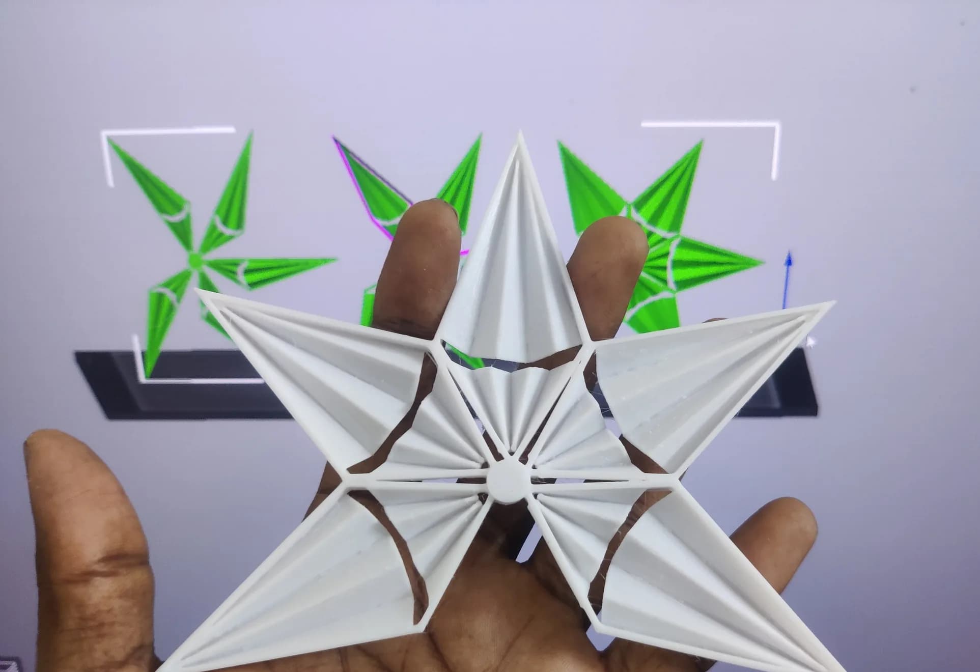 Printed star module held in front of a monitor showing the same star modules in green in CAD software