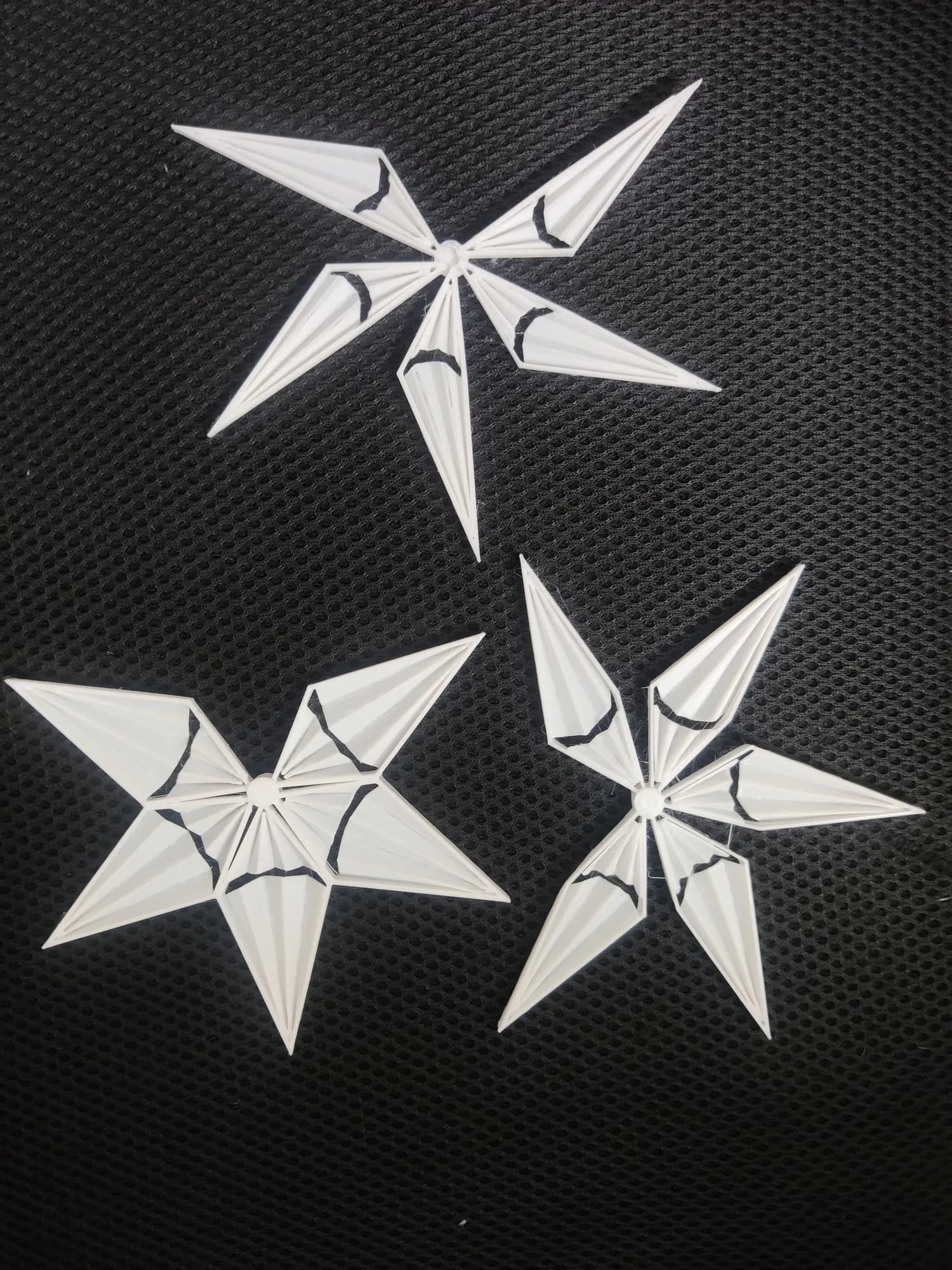 Three 3D printed six-pointed star modules with folded fins on a black mesh background