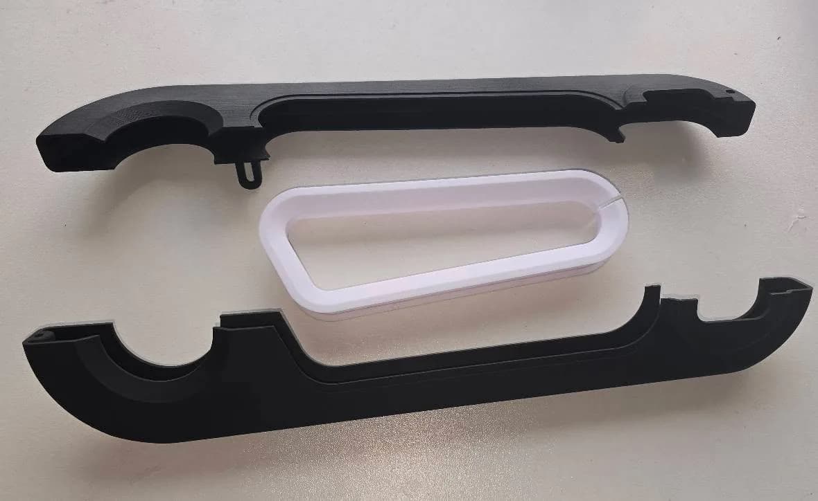 The bicycle chain cover taken apart: two black printed shells and the white window frame between them