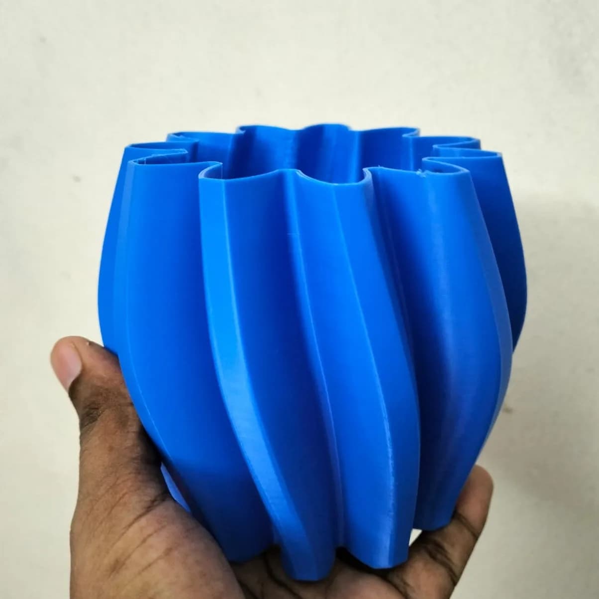 Hand holding the blue twisted vase, showing the smooth curved ribs