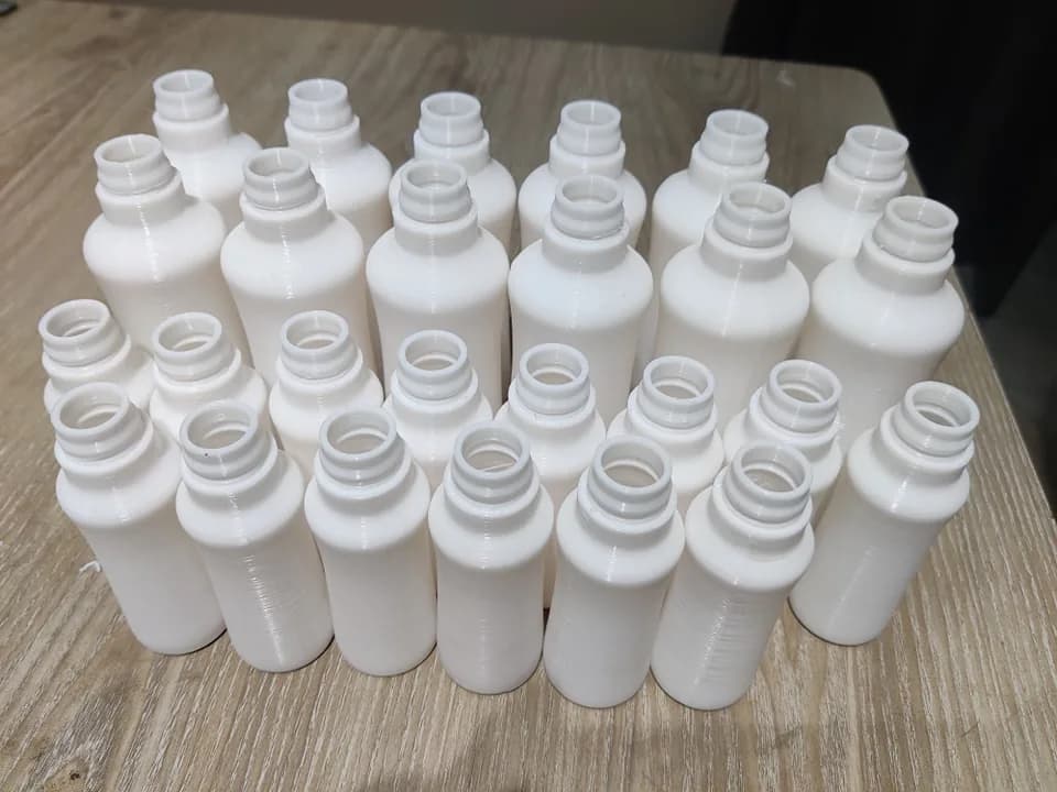 Close view of the white printed bottle prototypes from above, showing the ringed necks and openings