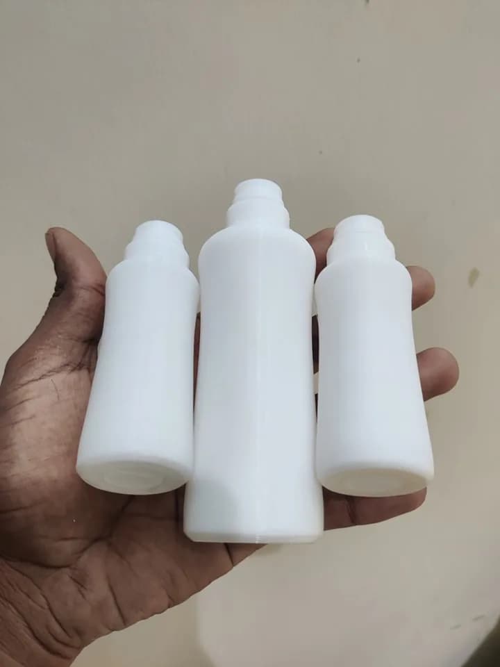 Hand holding three white 3D printed bottle prototypes, one tall and two shorter, showing the shoulders and stepped necks