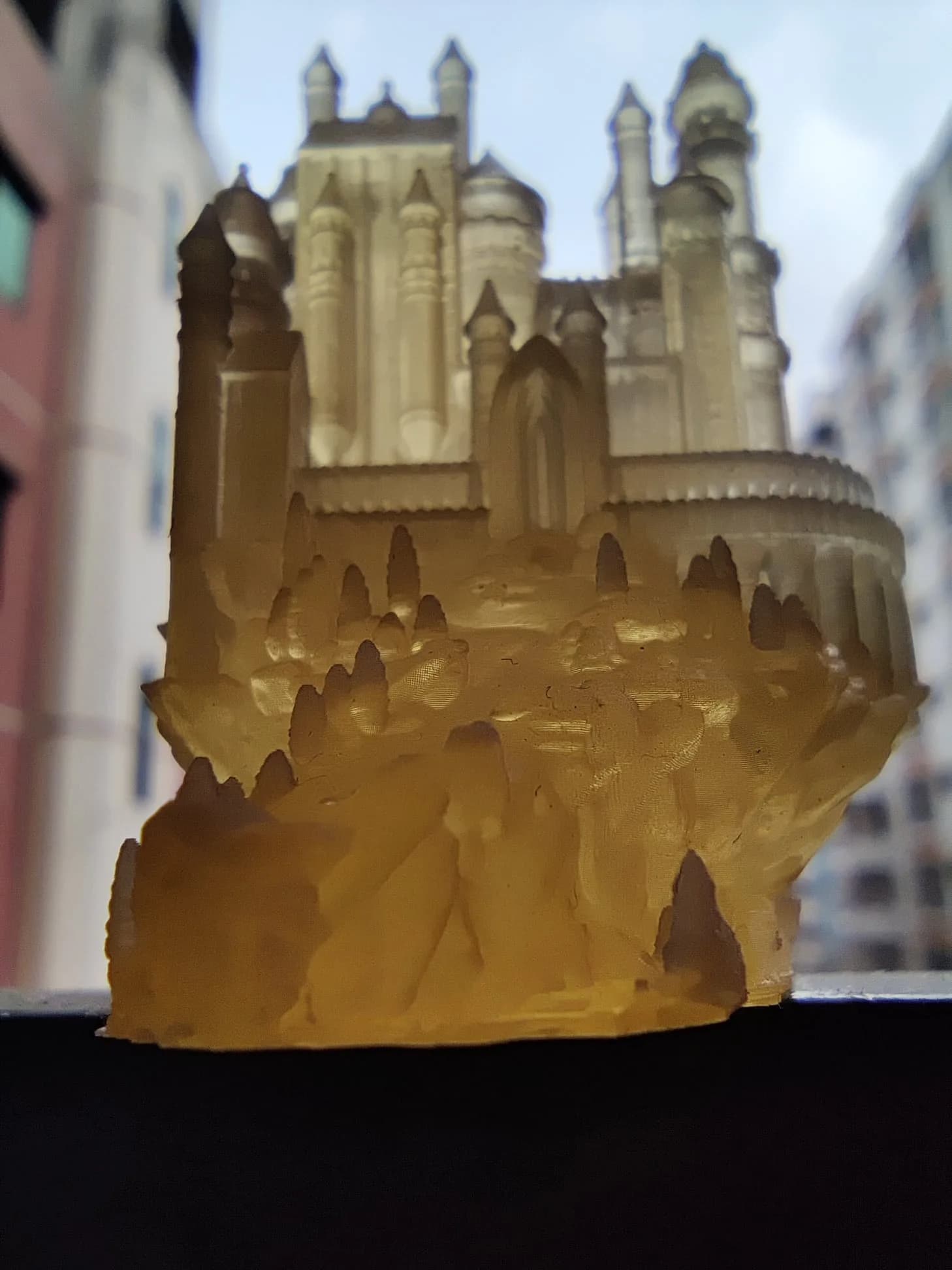 Close-up of the clear resin castle backlit by daylight, showing tower roofs, windows and the textured rock base