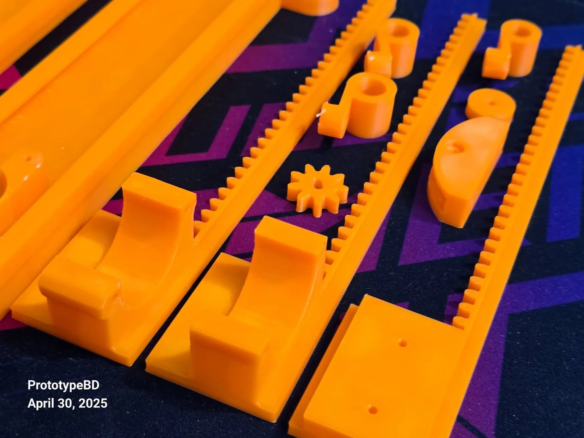 Close-up of orange 3D printed gear racks with fine teeth, a small pinion gear and curved saddles