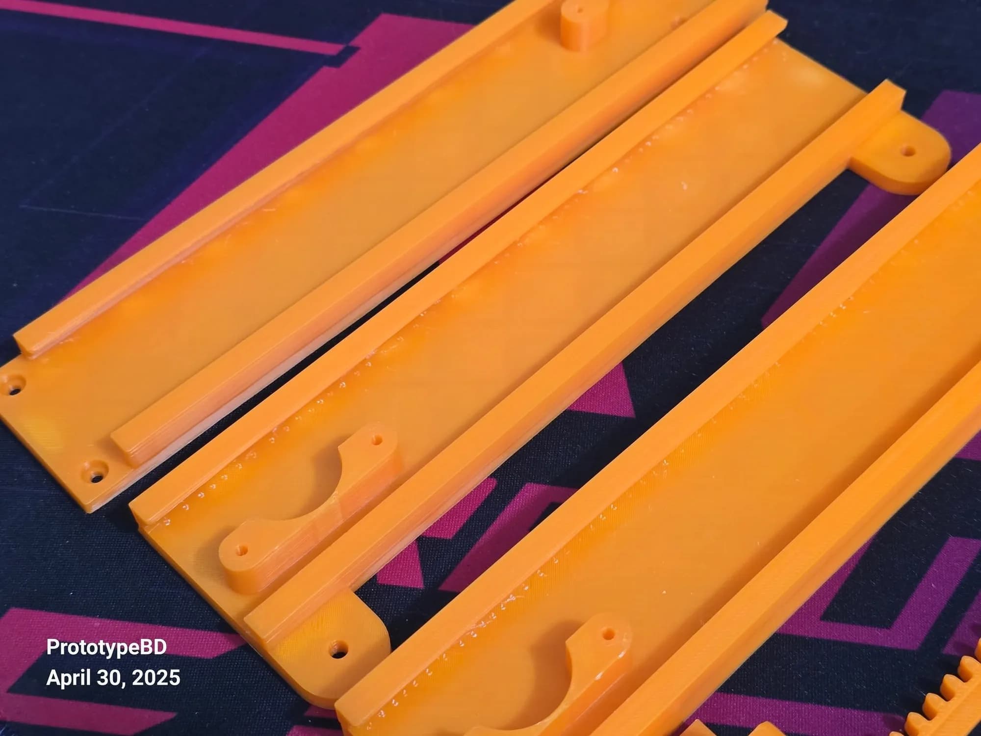 Angled view of orange 3D printed channel slide rails with screw holes, mounting ears and half-round clamps