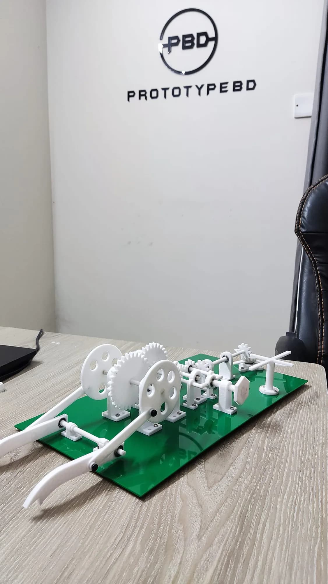 Side view of the assembled machine model on its green acrylic plate, curved arms in front and gears behind