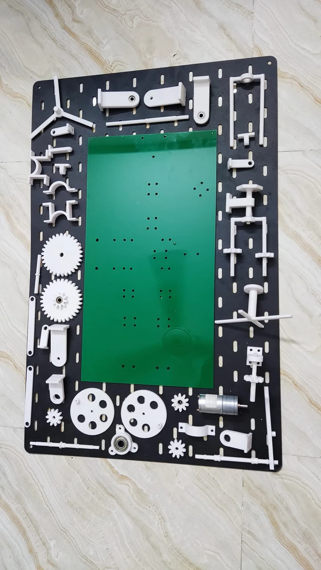 Green acrylic base plate with its hole pattern, surrounded by the printed gears, brackets, wheels and the motor before assembly