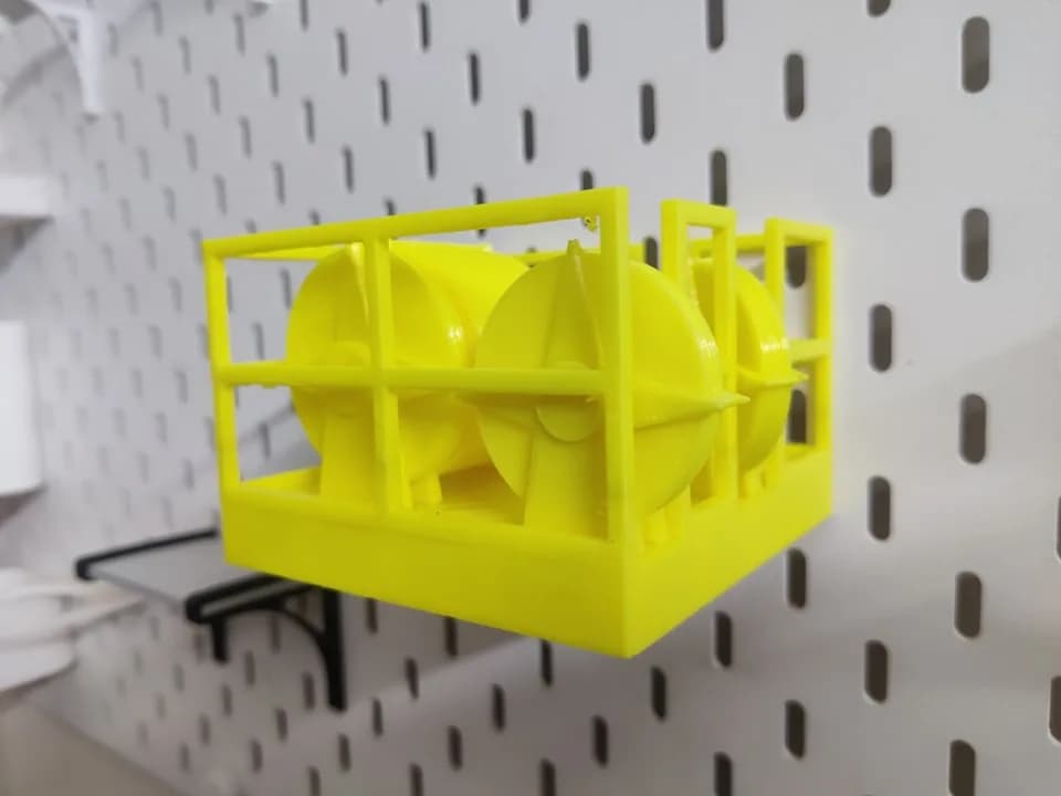 Yellow 3D printed crown block model on a white pegboard shelf, drums visible through the open railings