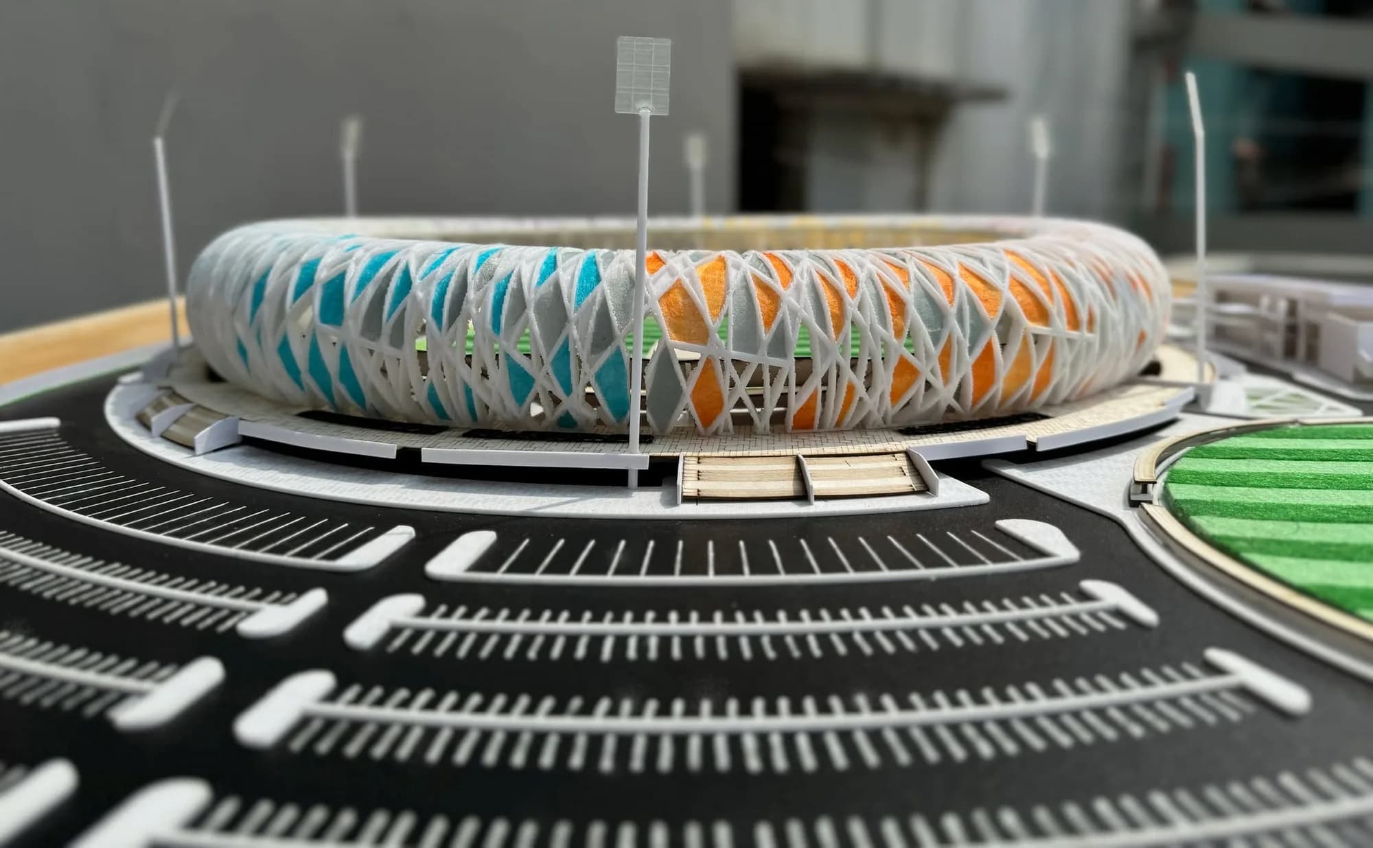 Car park rows in front of the stadium model, with blue and orange panels in the lattice shell