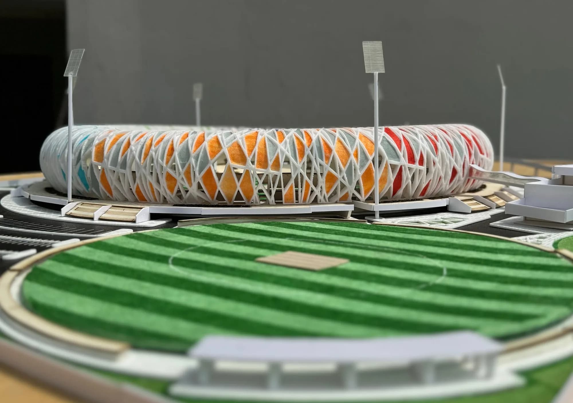 Stadium model seen across the practice ground, floodlight masts standing around the lattice bowl