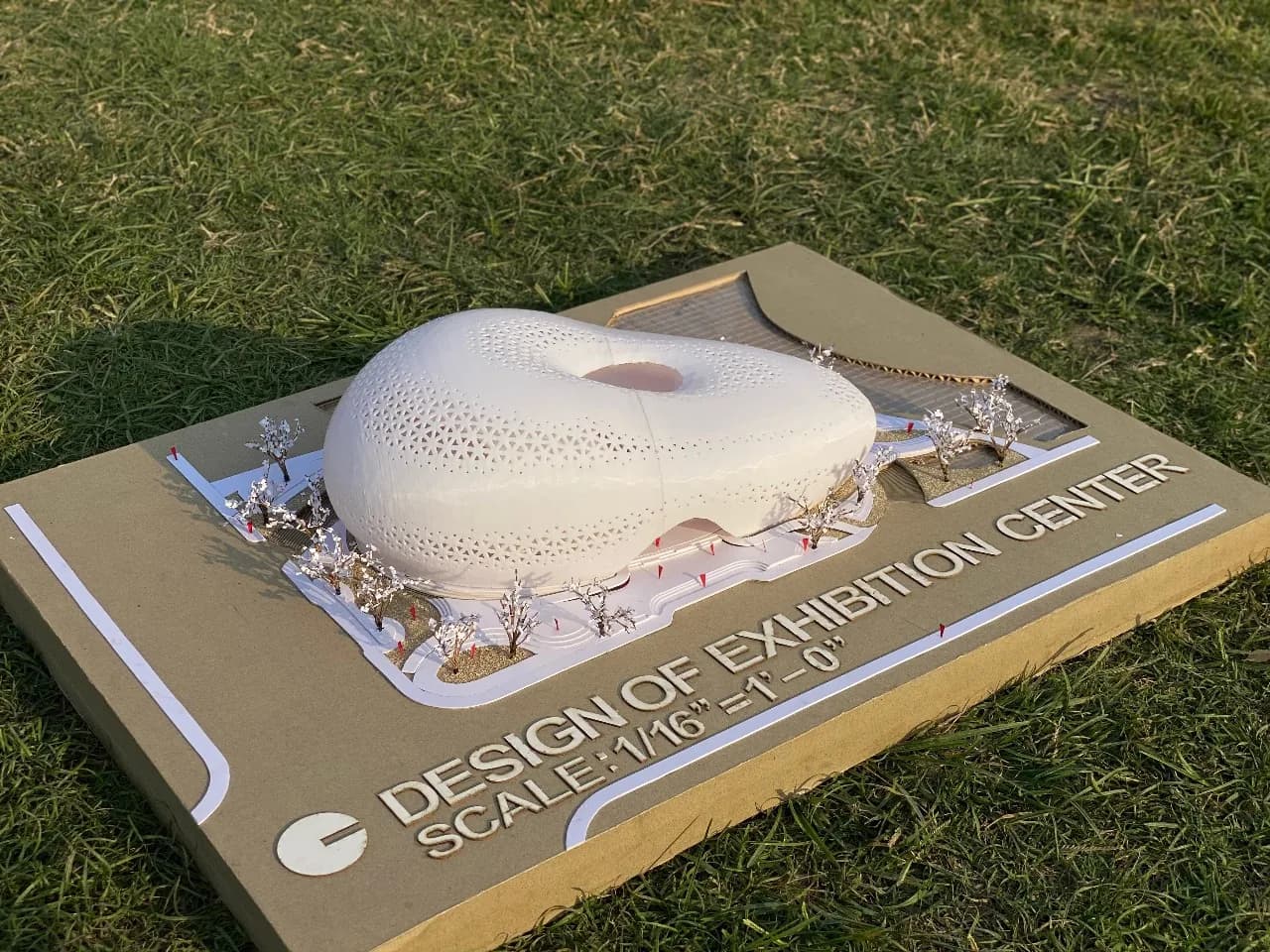 Angled view of the exhibition centre model on grass, showing the raised title letters and curved inlaid paths