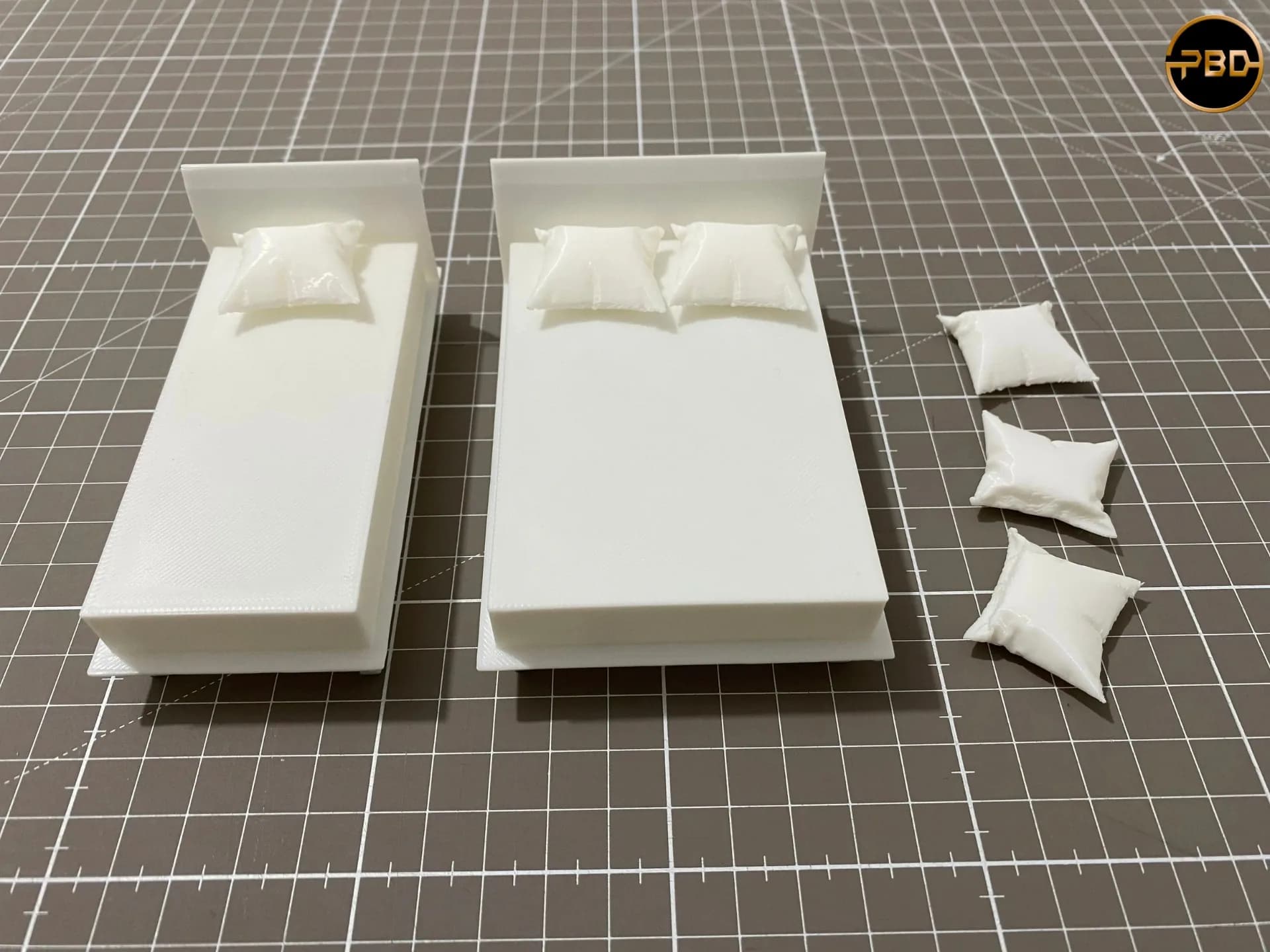 Two 3D printed miniature beds, single and double, with separate creased pillows beside them