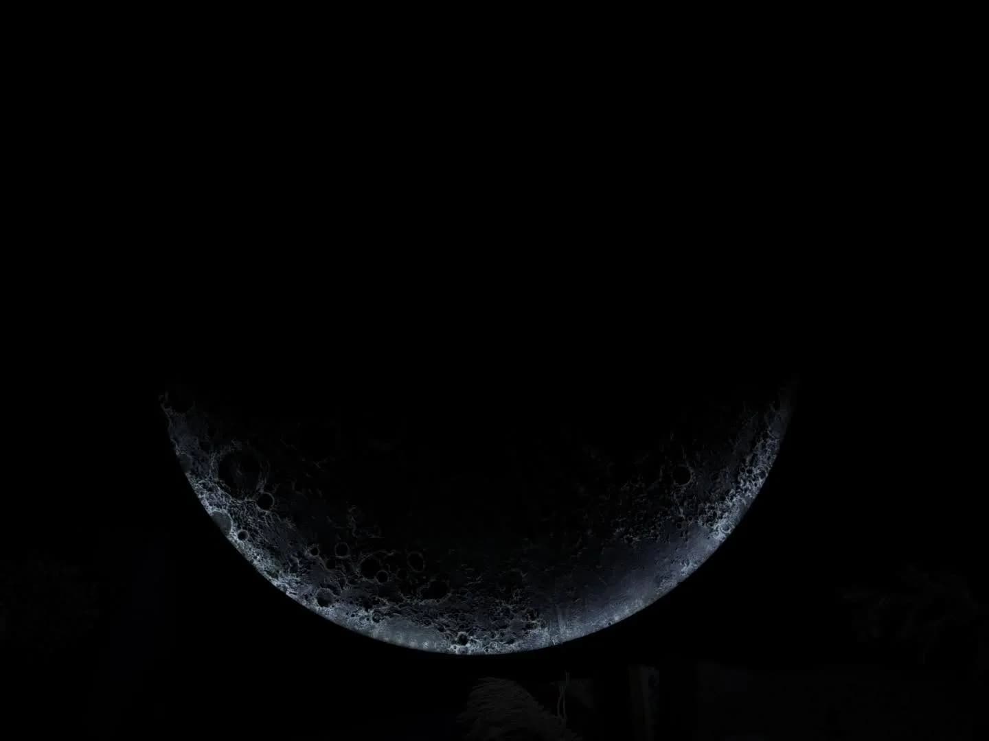 The moon lamp lit from one side so only a crescent of crater relief shows in the dark