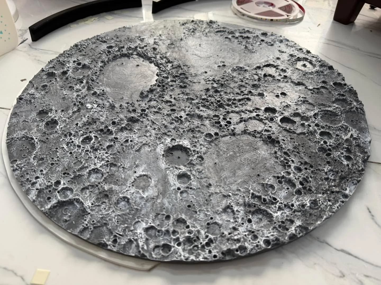 Moon relief after dry-brushing, white highlights on crater rims, with an LED strip reel and the ring frame beside it