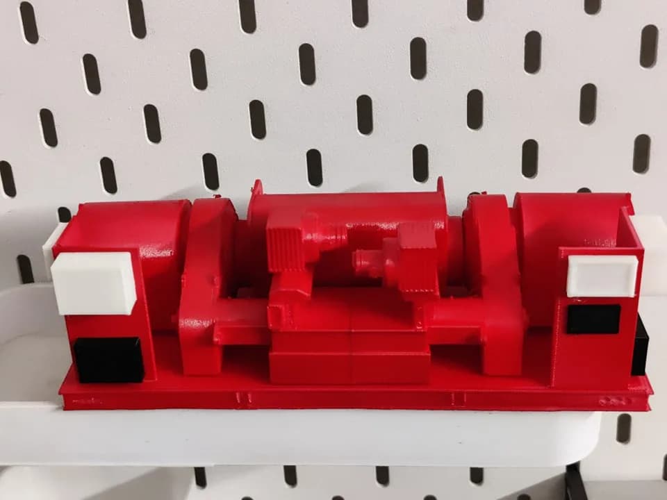 Rear elevation of the red oil-rig equipment model on a white pegboard shelf, with motor housings at both ends