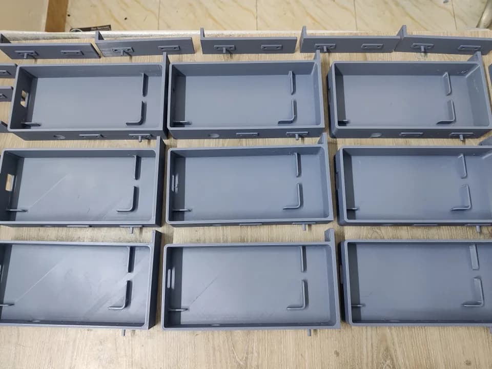 Top view of nine grey 3D printed trays with L-shaped retaining clips, with matching side rails along the top