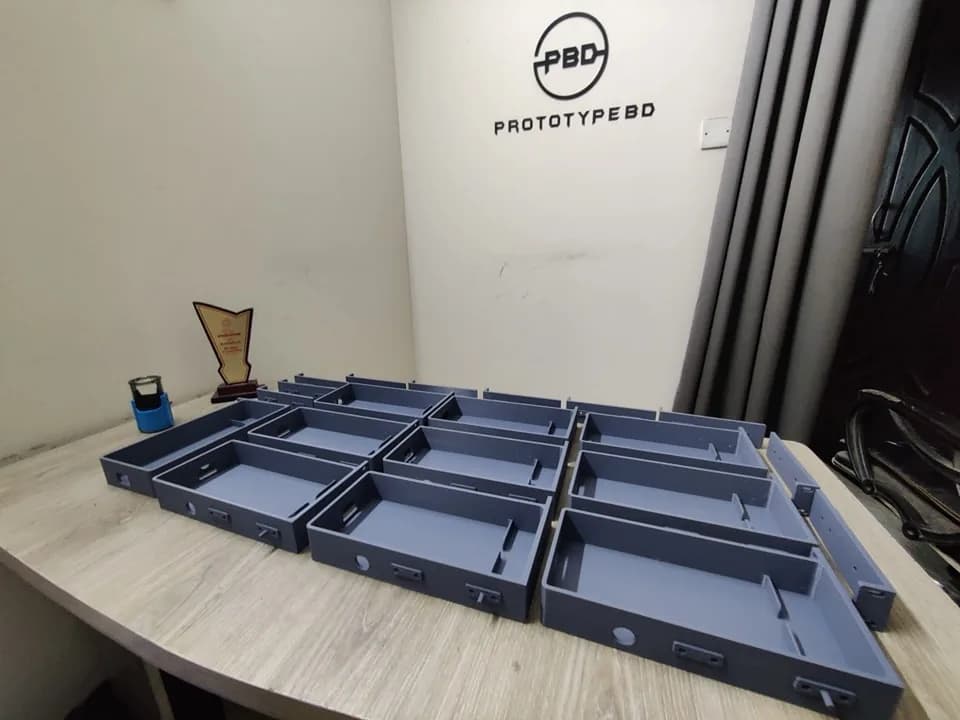 Batch of grey 3D printed rack mount trays and rails on a table in the PrototypeBD workshop