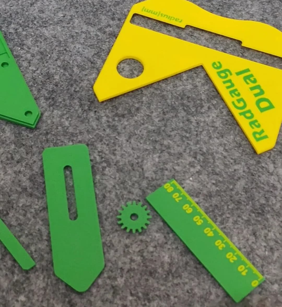 Loose 3D printed radius gauge parts: a yellow body, a green slotted slider, a small green gear and a green scale strip