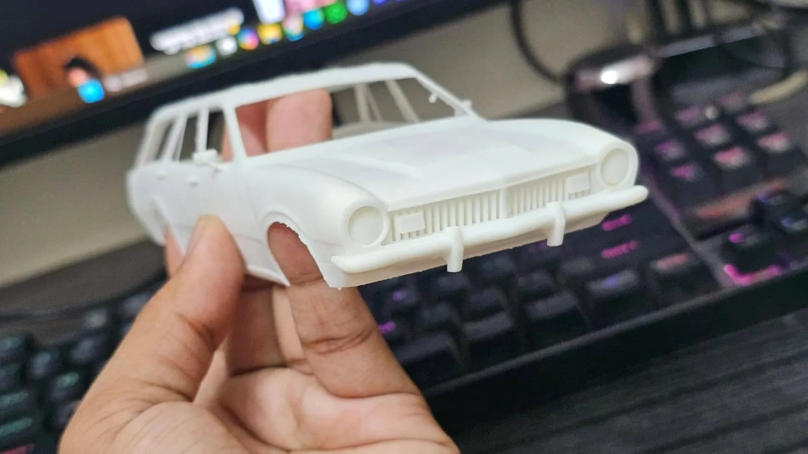 Hand holding the resin car body, front view of the slatted grille, bumper and round headlights