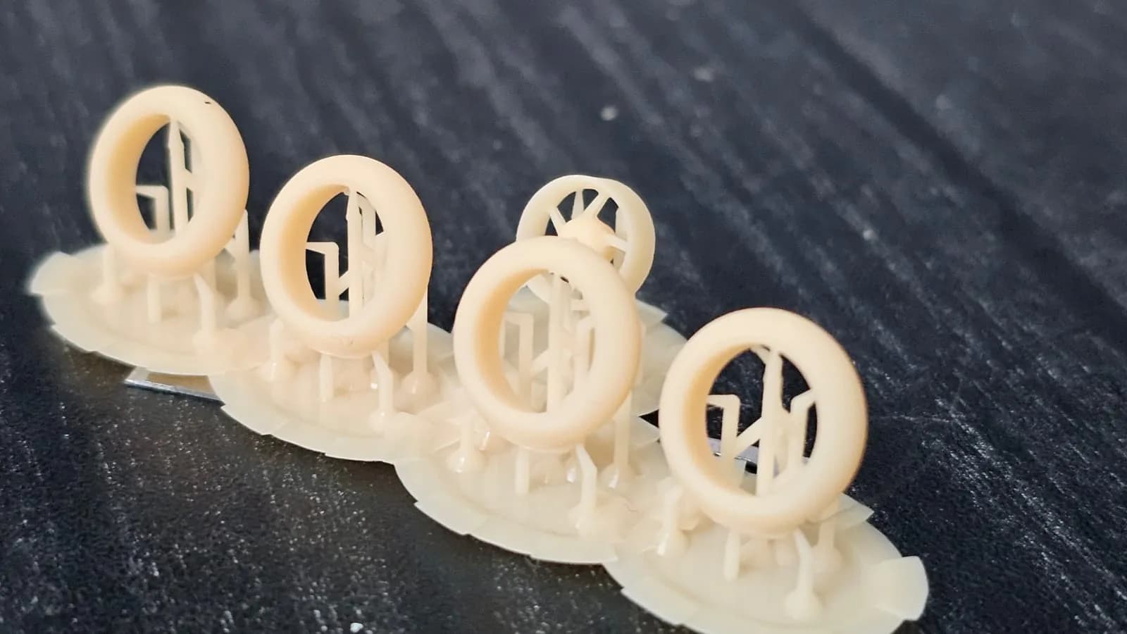 Five small resin-printed motorcycle wheels standing upright on thin support structures after printing