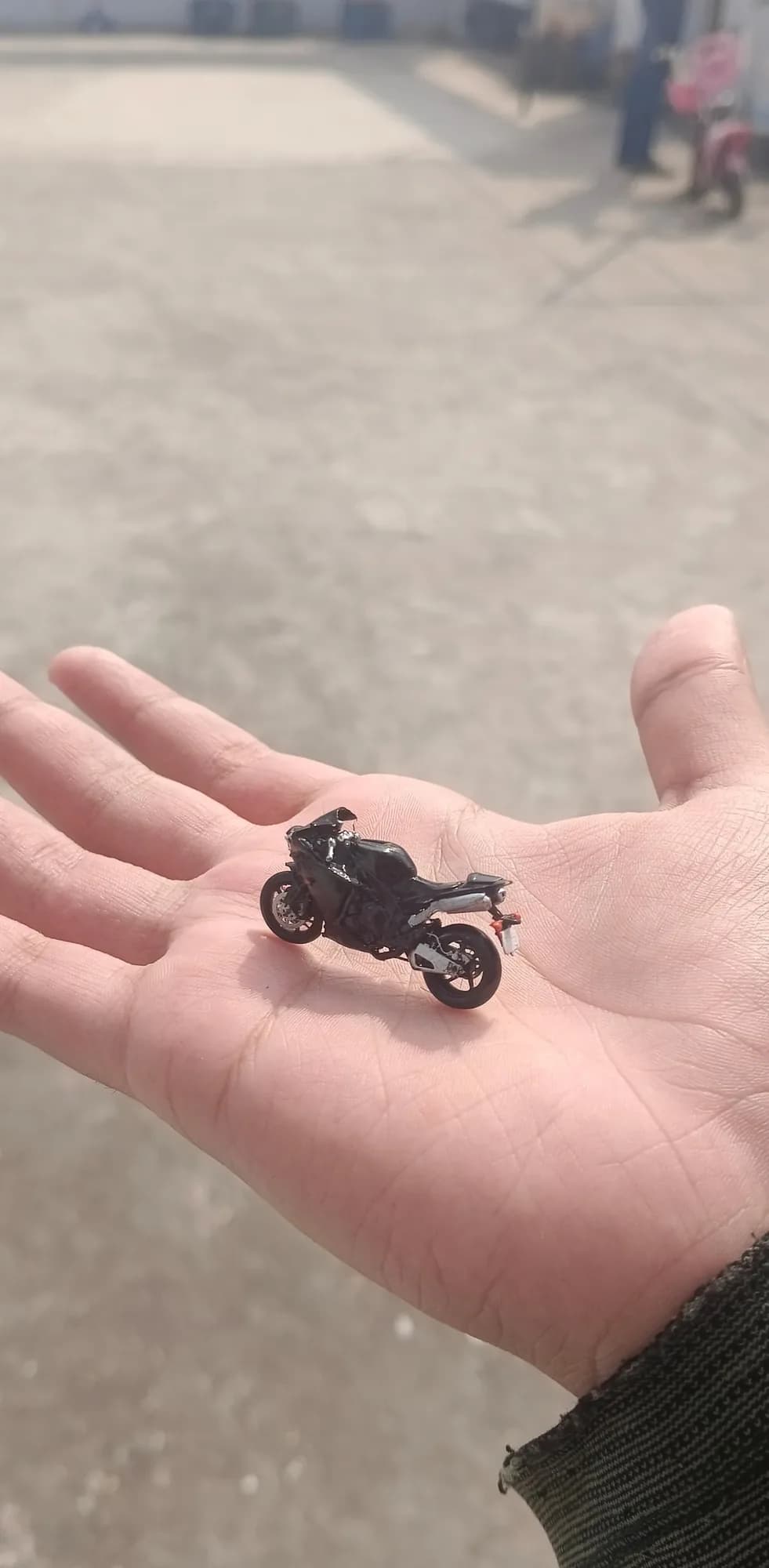 Resin sport bike miniature on a palm outdoors, shot from above to show the seat and tail