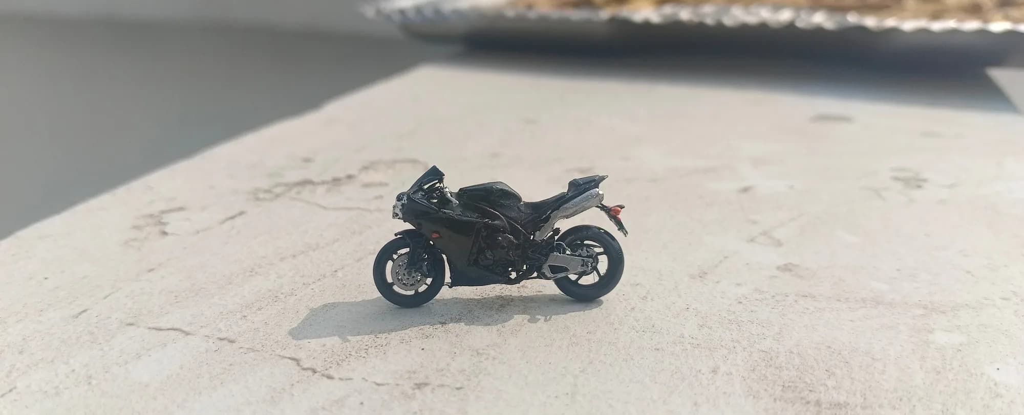 Miniature sport bike on a concrete ledge, side profile with brake disc and swingarm visible