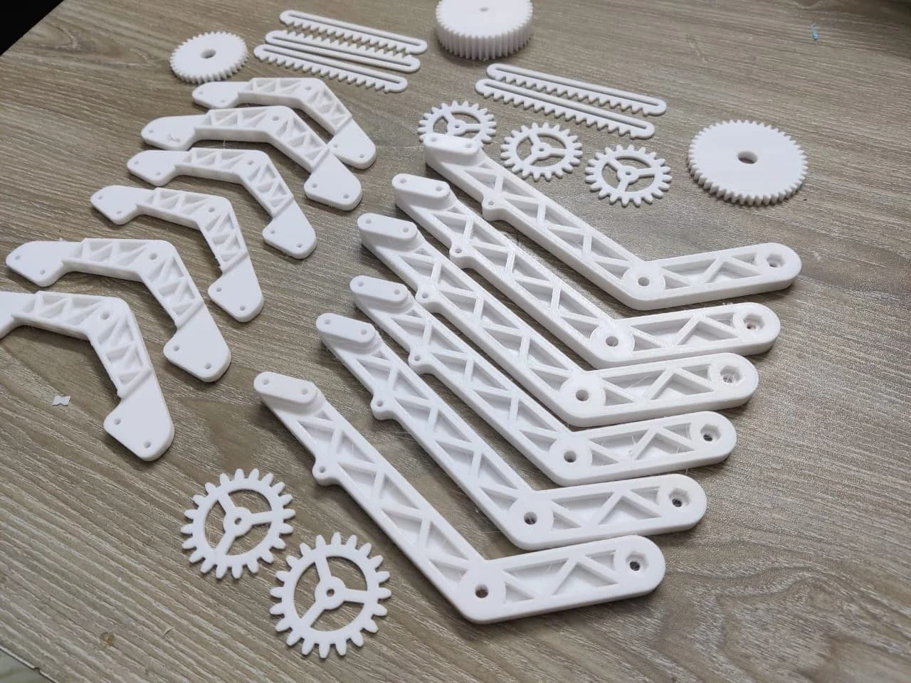 Angled view of white 3D printed rover arms with pivot holes, spoked gears and gear racks
