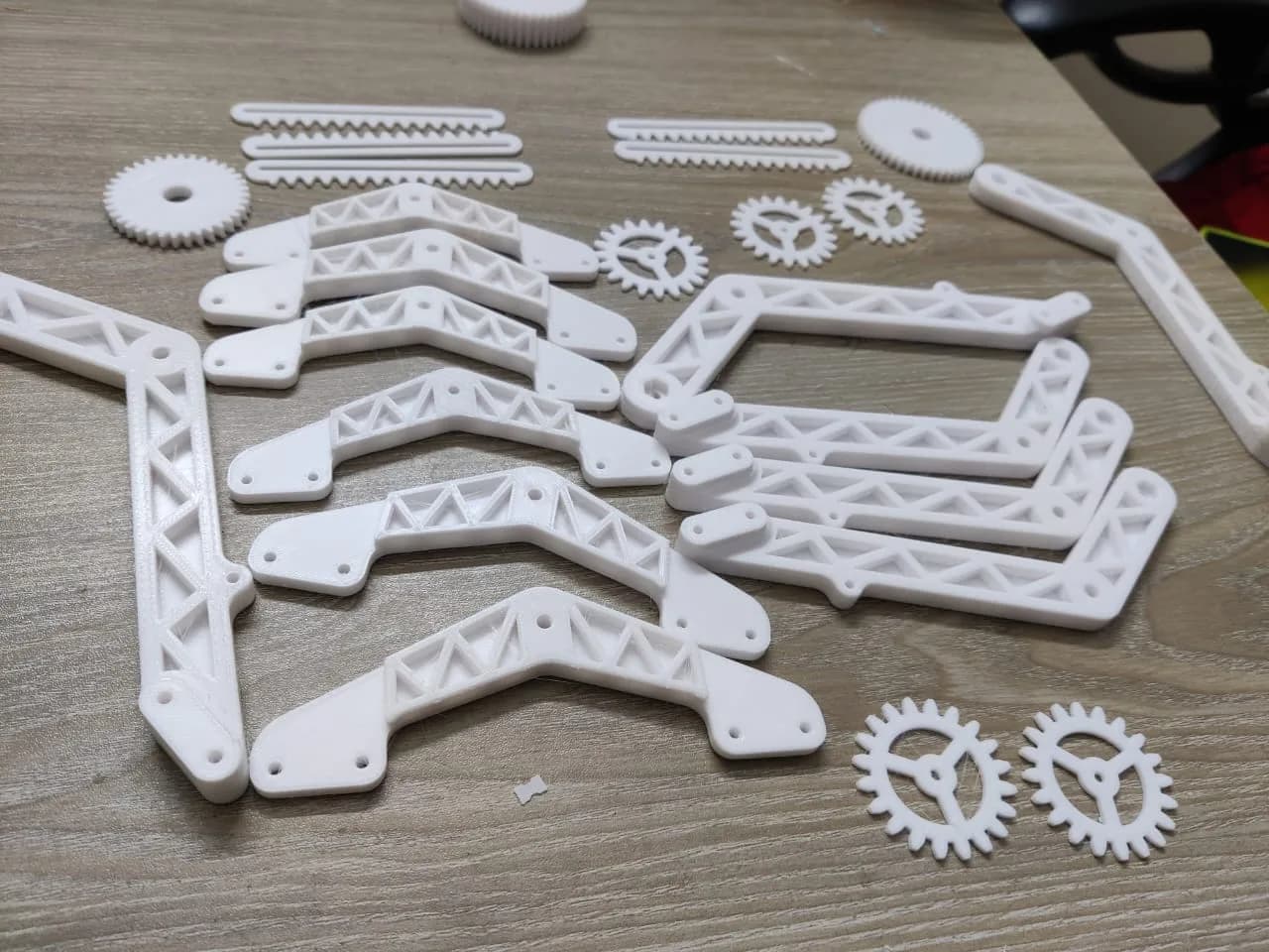 Batch of white 3D printed Mars rover suspension arms and gears seen at a low angle