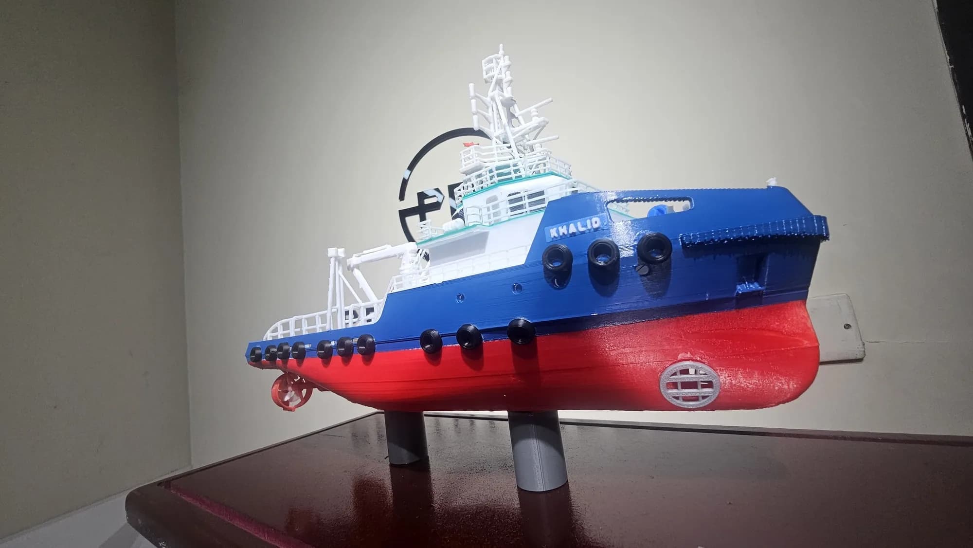 Low-angle view of the tugboat model's bow with the name KHALID, black fenders and a red lower hull