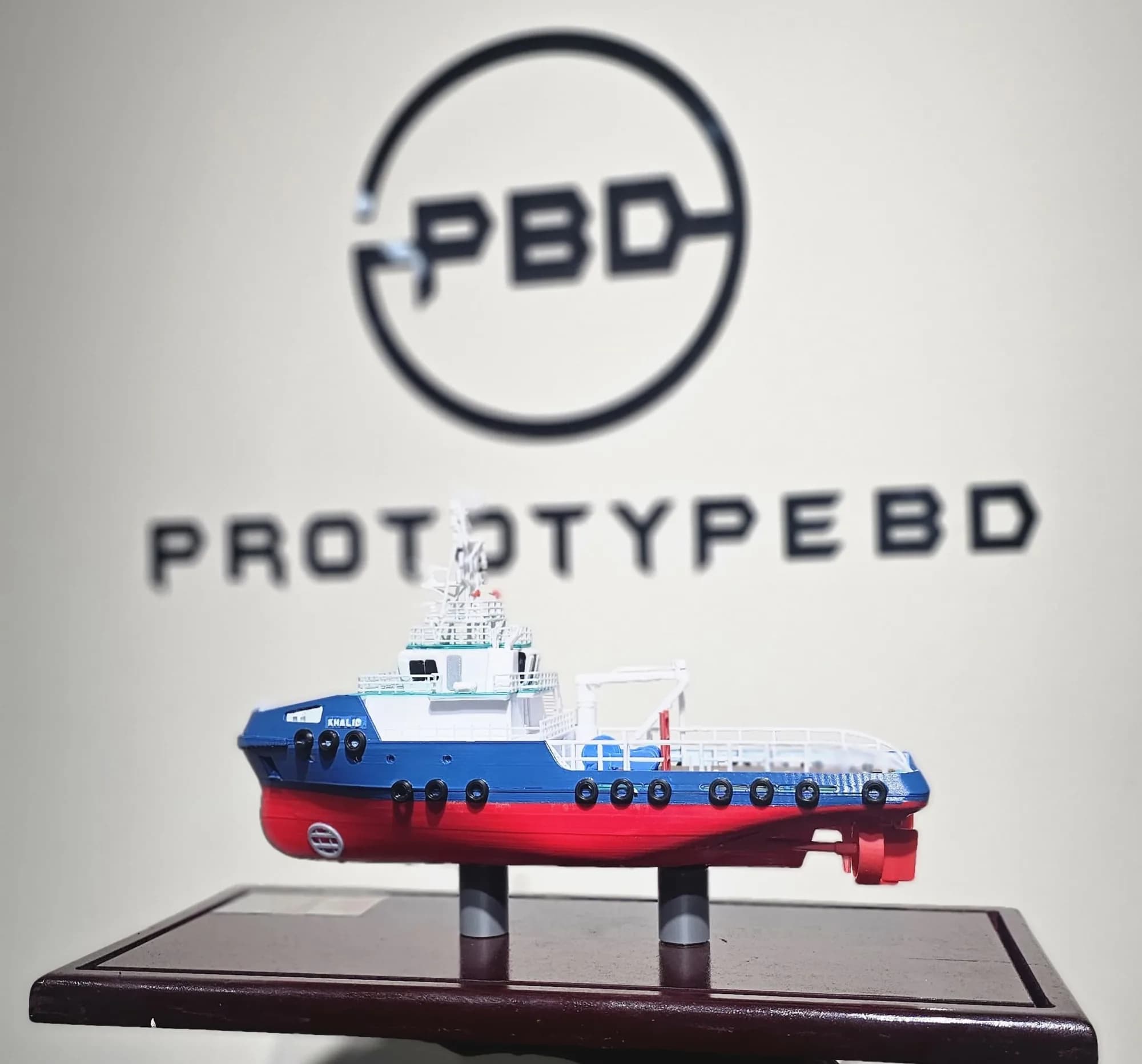 Side profile of the tugboat model with the PrototypeBD logo behind it, showing the propeller and rudder under the stern