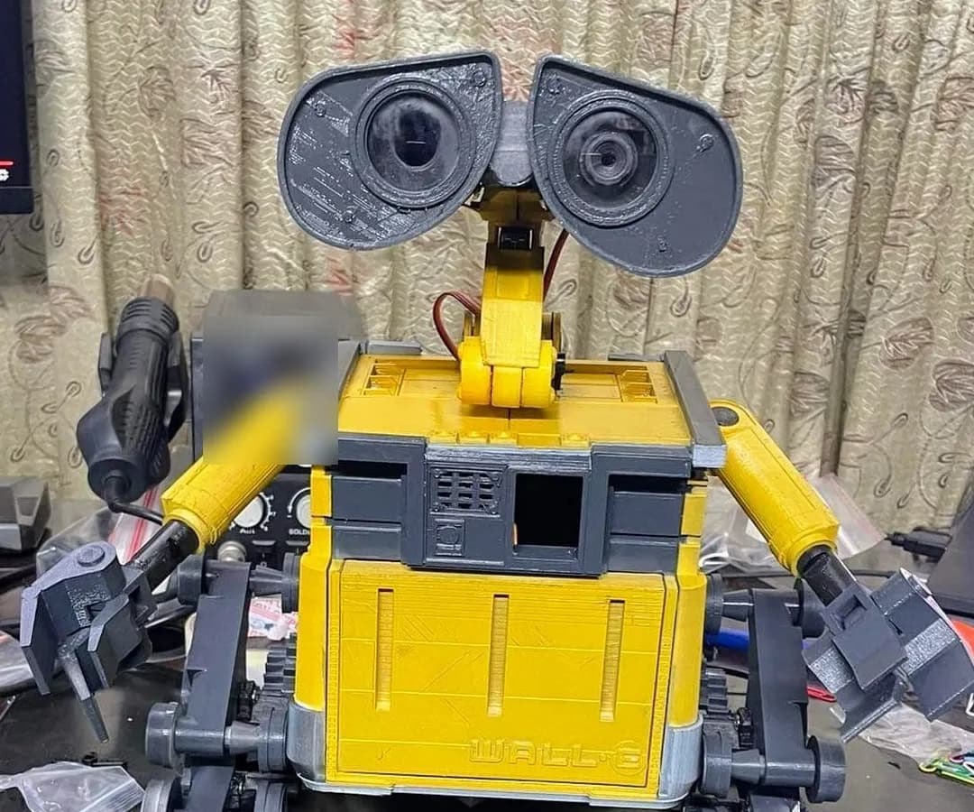 Front view of the life-size WALL·E replica with both arms out, binocular eyes raised and the name embossed on the body