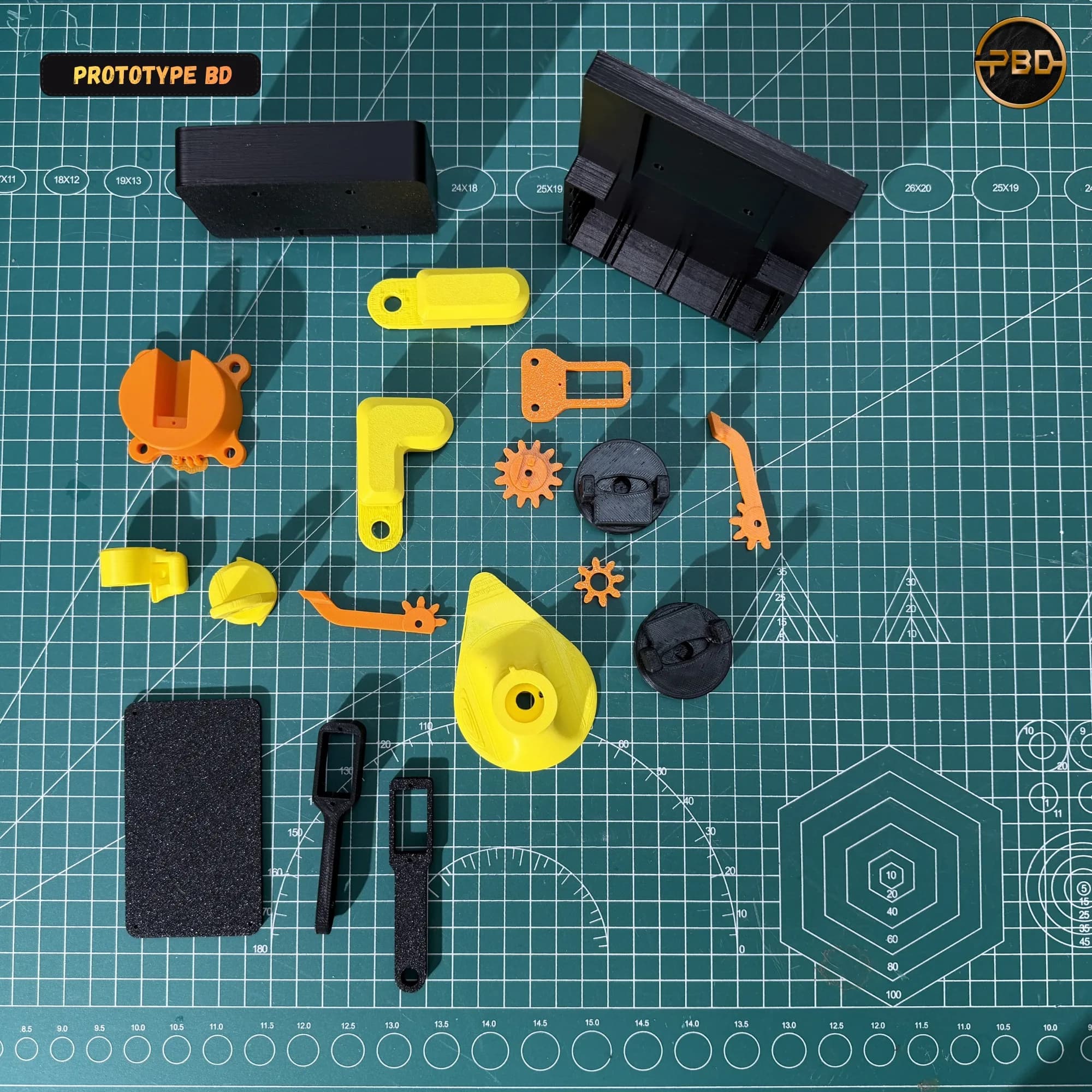 Flat lay of the 3D printed robotic arm parts in black, orange and yellow on a green cutting mat: base housing, links, gears, gripper parts and cover plate