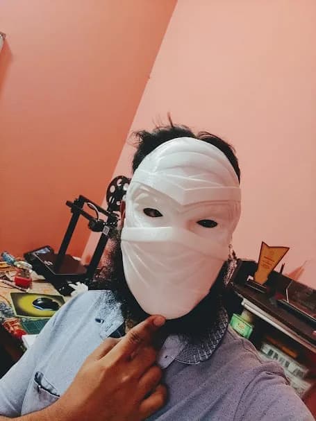 The white mask worn for a fit test in the workshop, face fully covered, a 3D printer behind