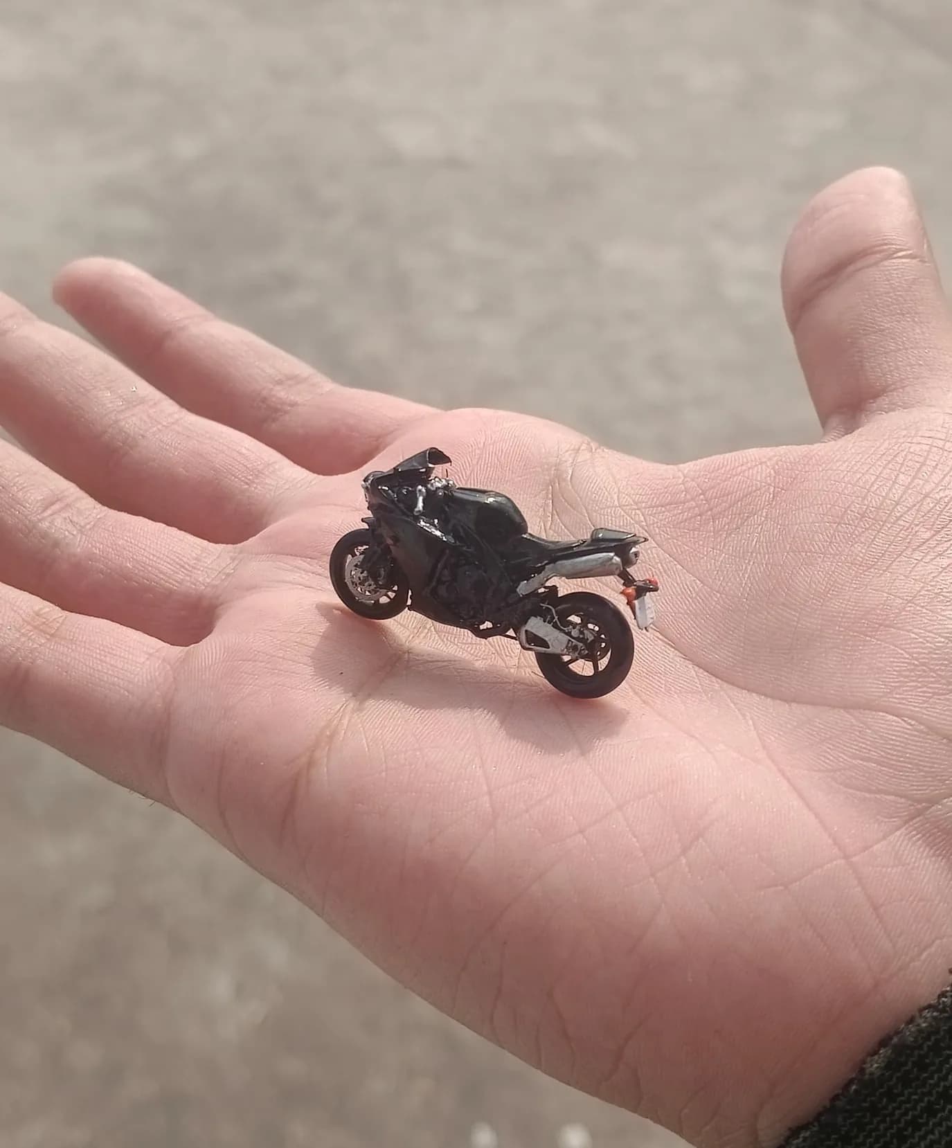 Miniature resin sport bike standing in the middle of an open palm, showing its small size