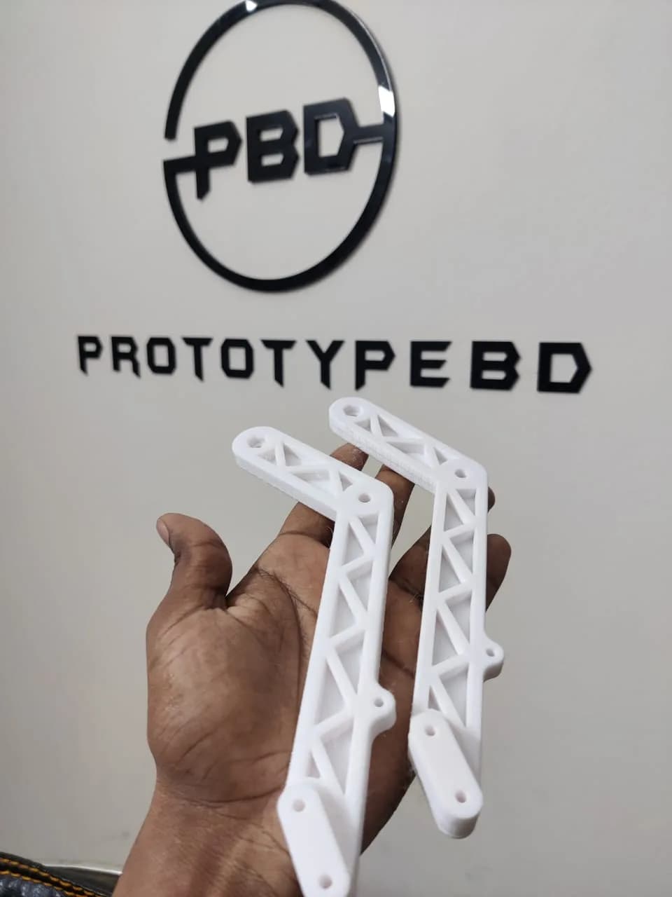 Hand holding two white 3D printed rocker-bogie arms with a triangulated truss pattern