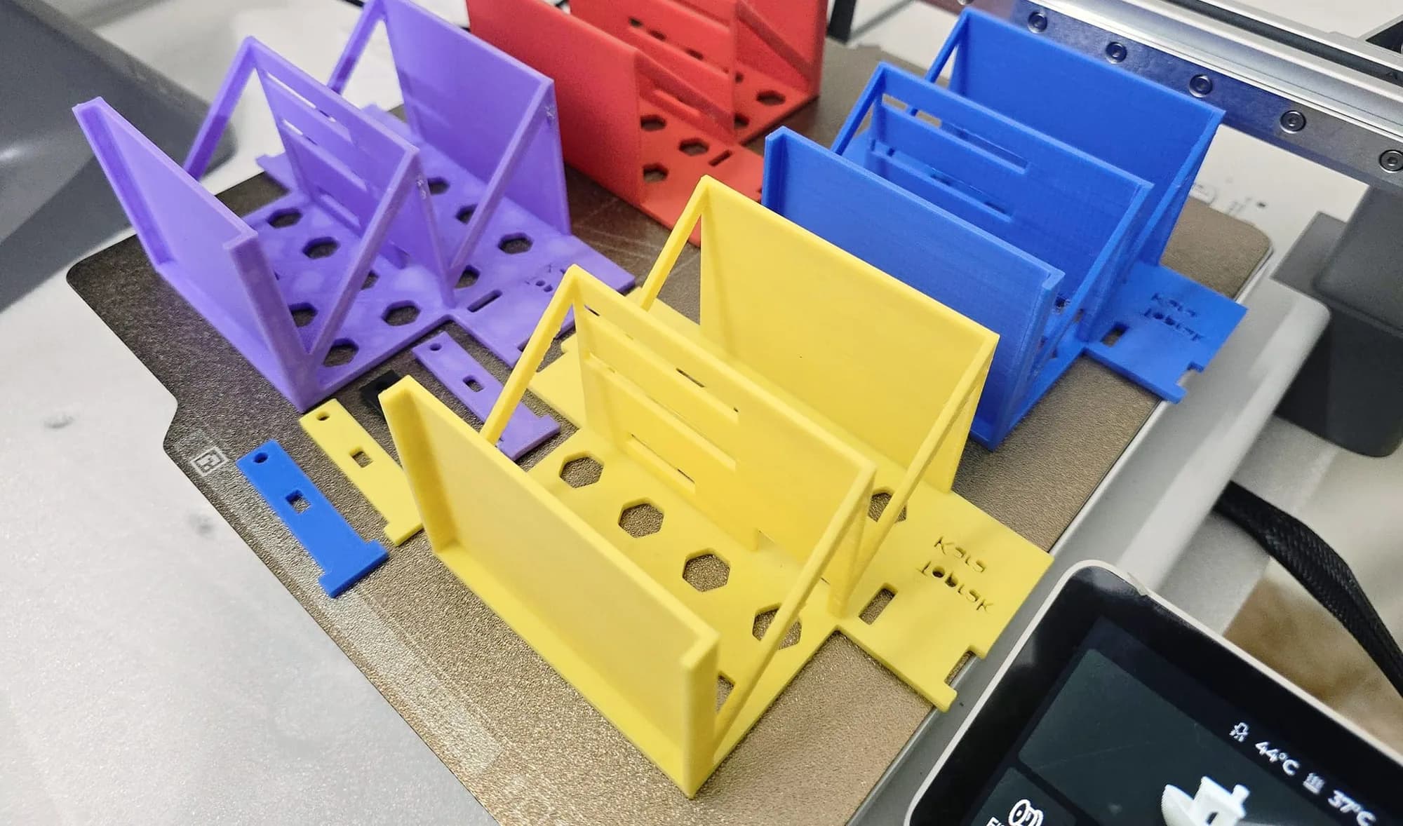 Purple, red, yellow and blue self-balancing robot body parts still on the 3D printer build plate after printing