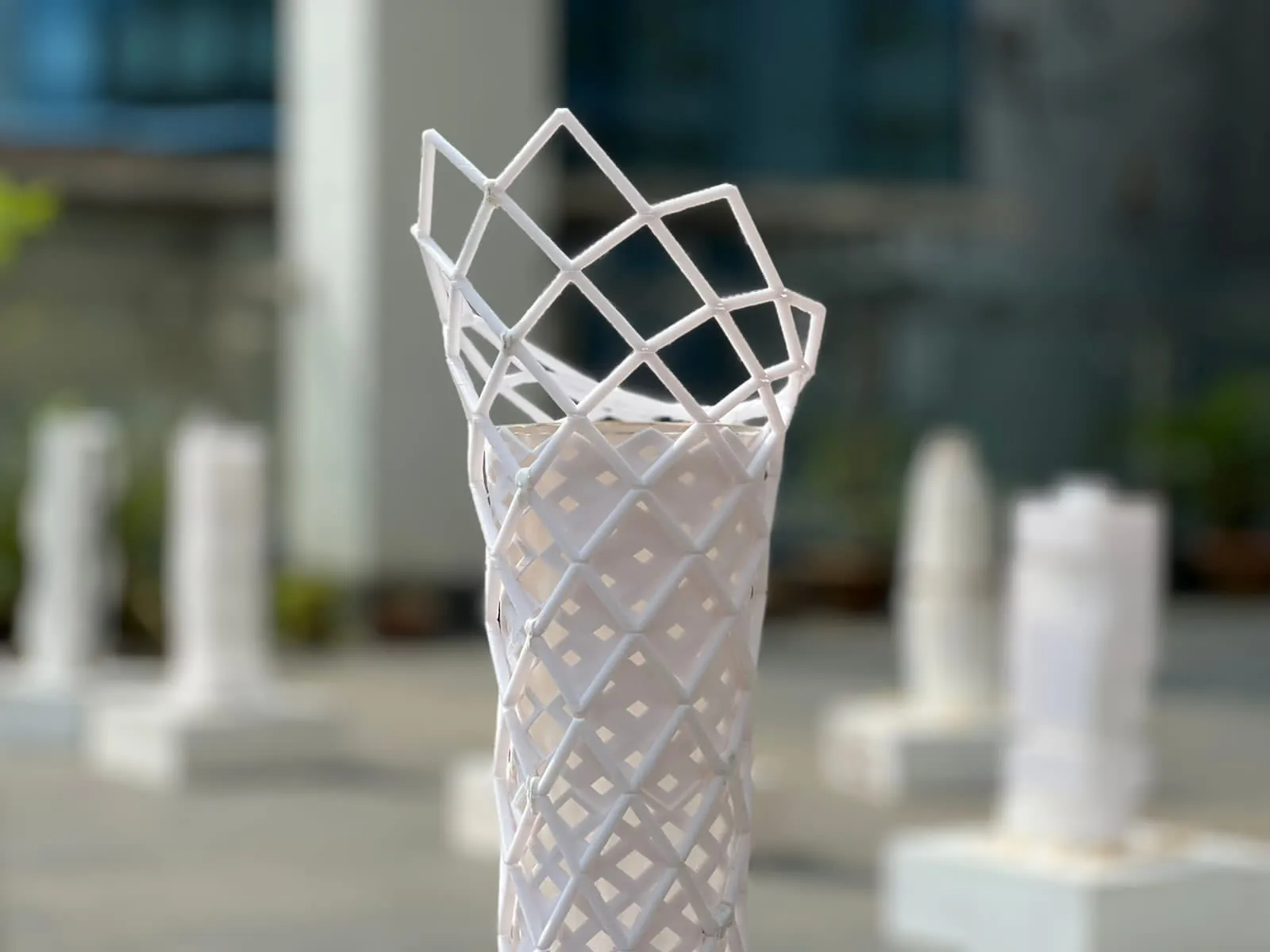 White 3D printed tower model with an open diamond lattice crown, other tower models blurred behind