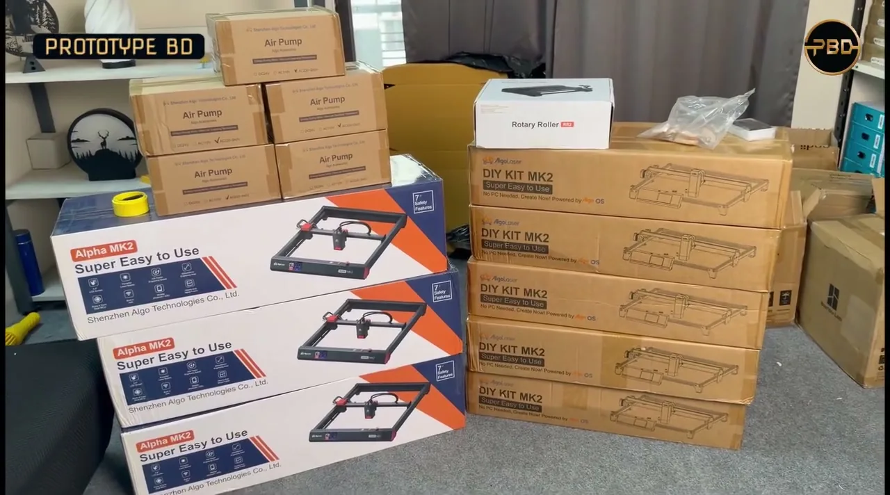 Stacked AlgoLaser Alpha MK2 and DIY KIT MK2 engraver boxes, air pumps and a Rotary Roller in the PrototypeBD stock room