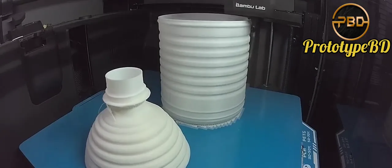 Two white 3D printed bottle sections, a ribbed shoulder piece and a ribbed cylindrical body, on a printer bed