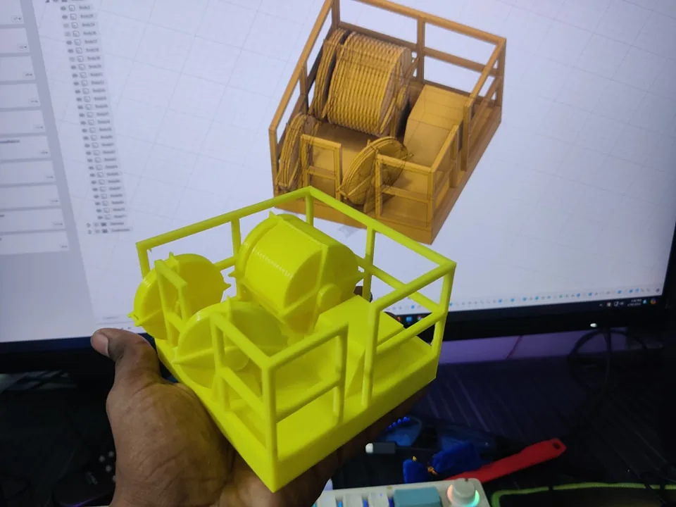 Yellow 3D printed crown block model held in front of a monitor showing its CAD assembly