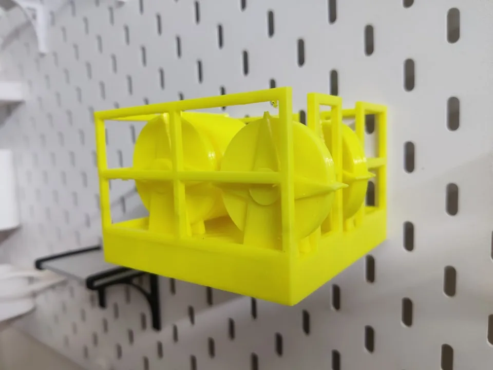 Yellow 3D printed crown block model with sheaves and guard rails displayed on a pegboard shelf