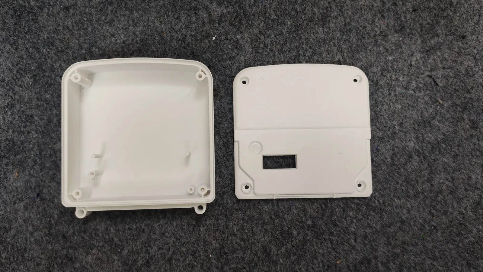 White 3D-printed IoT gas meter housing halves: corner screw bosses, bottom mounting ears and a cover with display window