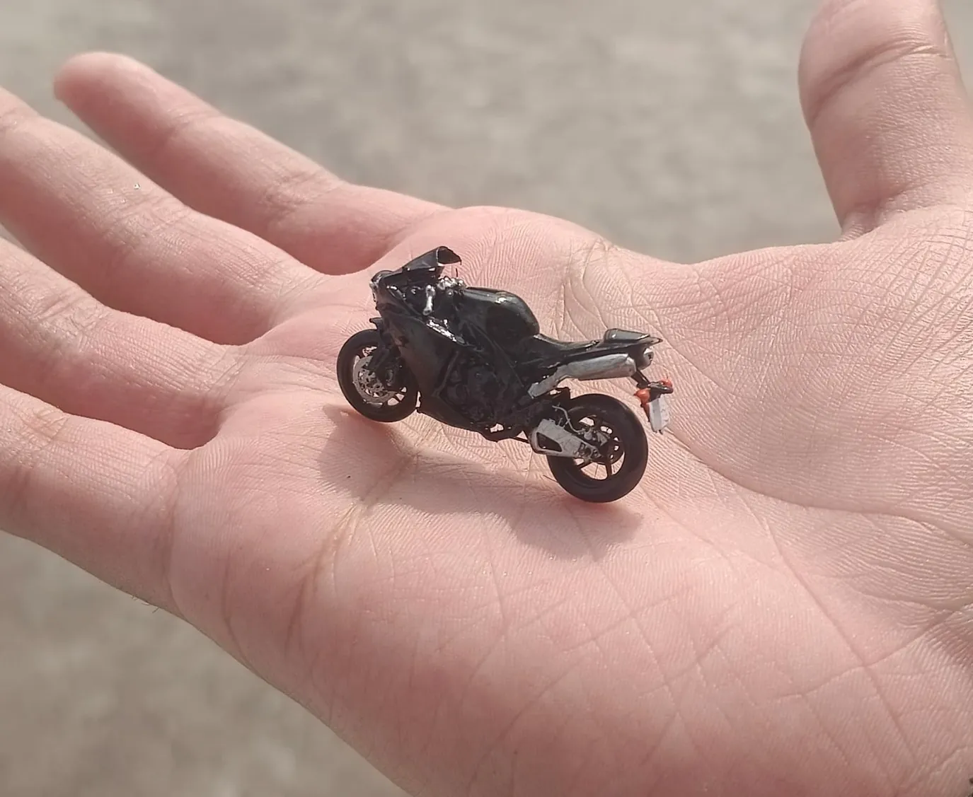 Small black resin 3D printed miniature motorbike resting in the palm of an open hand