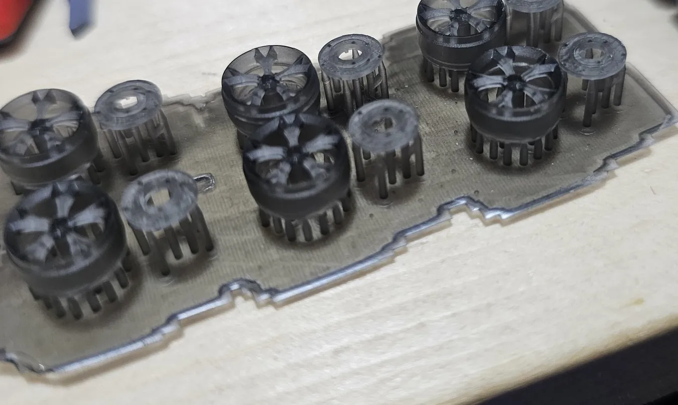 Smoky grey resin printed model car wheels and hubs still standing on support pillars on a clear resin raft