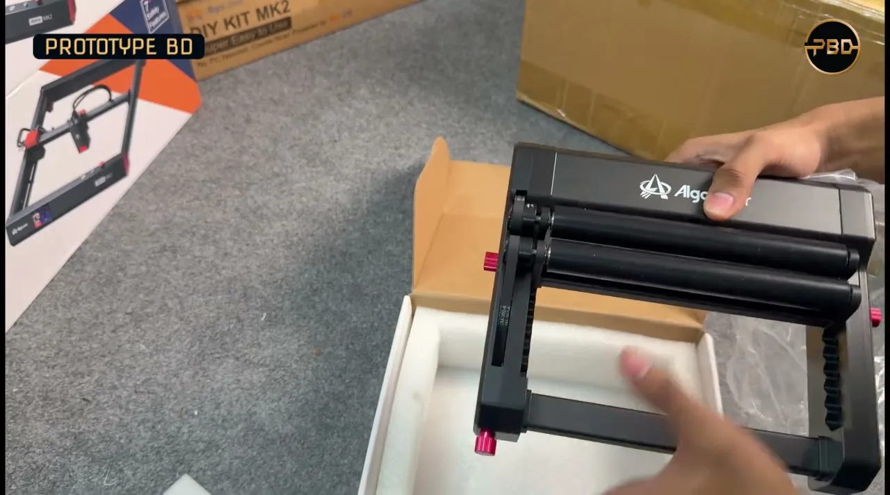 Hands lifting a black AlgoLaser rotary roller out of its foam-lined box