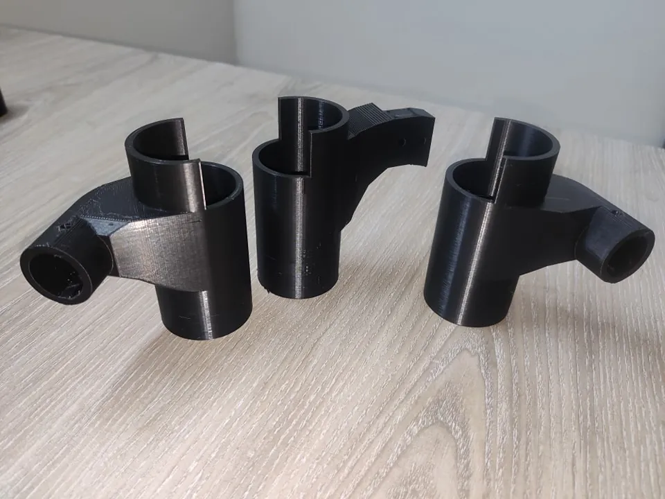 Three black 3D printed tube connector brackets with slotted round collars for a rover frame, on a wooden table