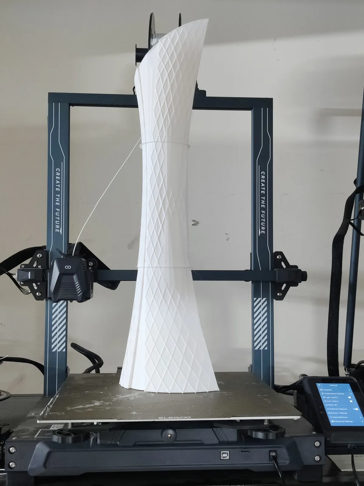 Tall white tower model with a diamond facade pattern standing on a 3D printer bed