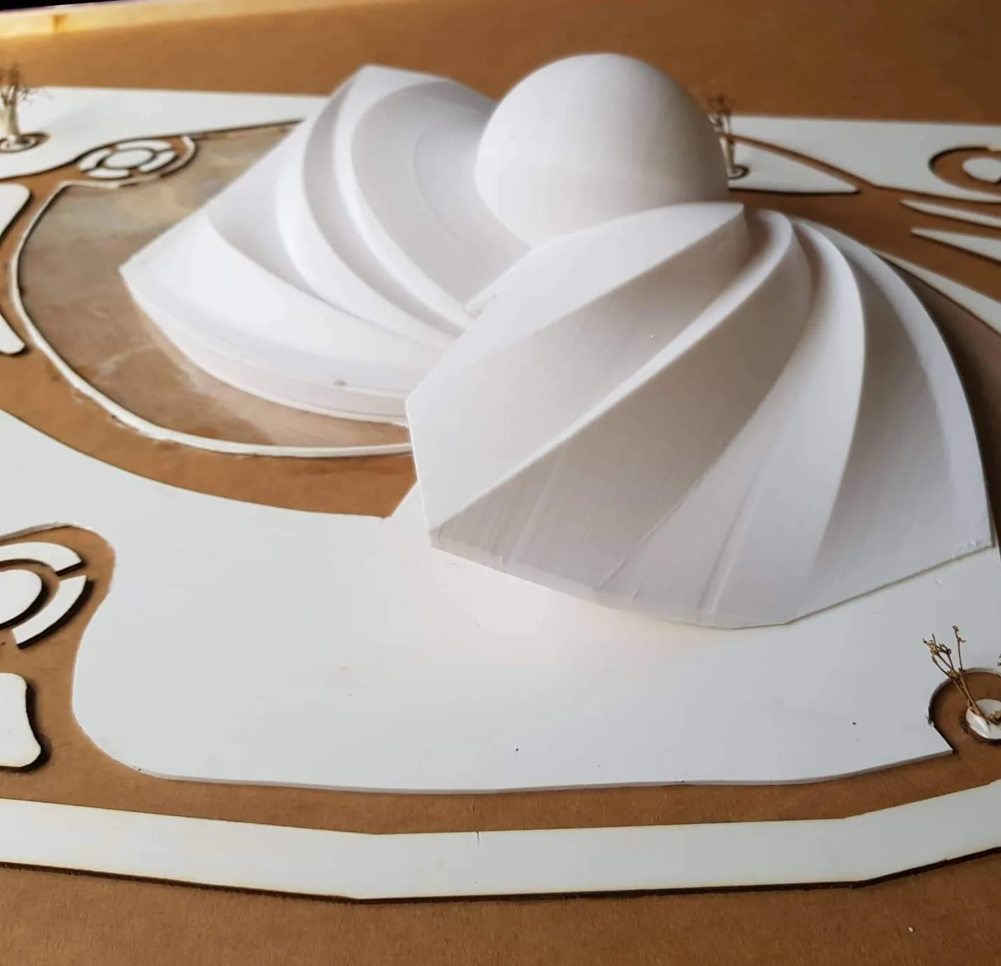 White 3D-printed shell roofs and a dome sitting on a layered white and brown site board, seen from above