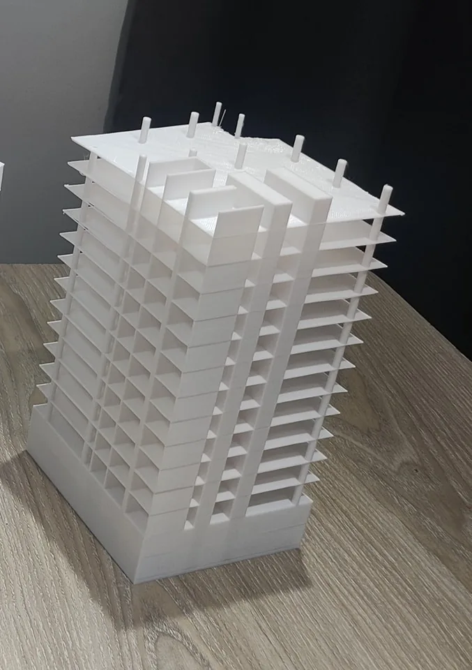 Close-up of a white 3D printed high-rise model showing stacked flat floor slabs, columns and a few loose strands on the roof